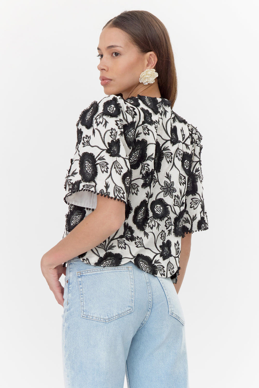 Back view of model wearing white, short-sleeve blouse with black, floral lace and buttoned neckline.